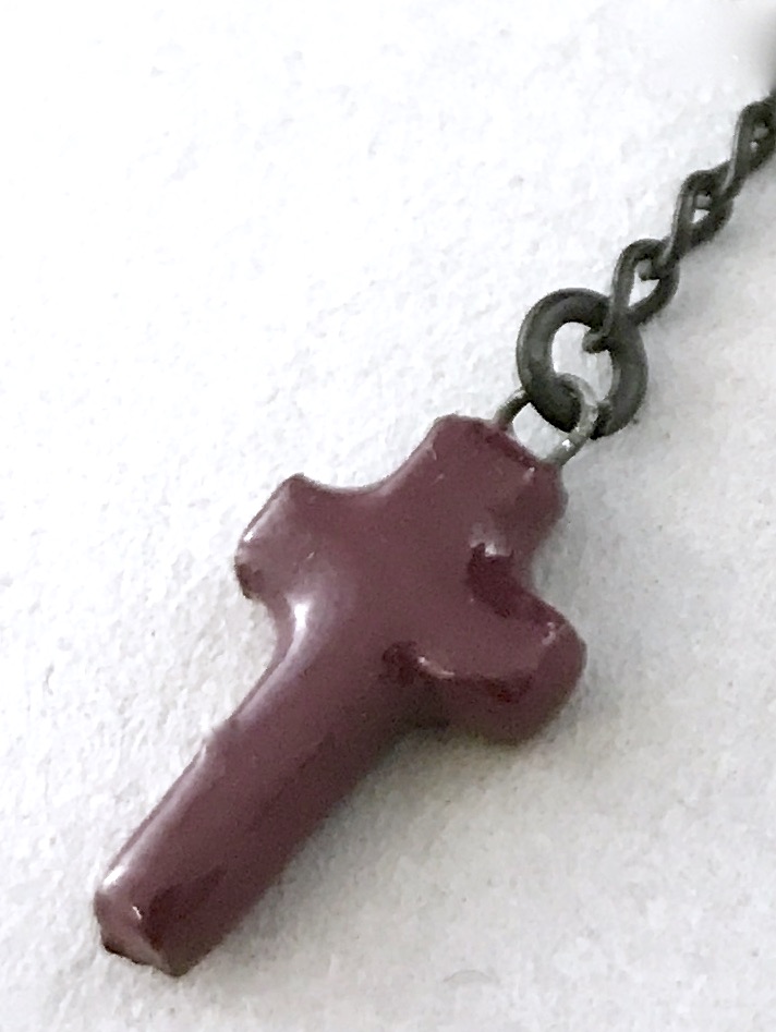 Boucles d'oreilles formée d'une croix en céramique suspendue à une longue chaine sombre.
