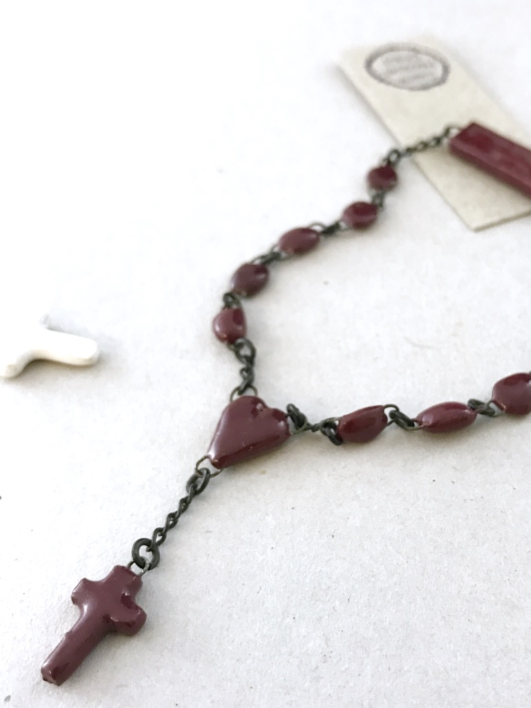 Bracelet de céramique aux perles miniatures, une mini croix de même matière est accrochée par un sacré coeur au bracelet.