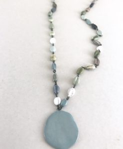 Collier mi long en céramique formé de perles en formé de cauris en faience et terminé par une pastille de meme matière.