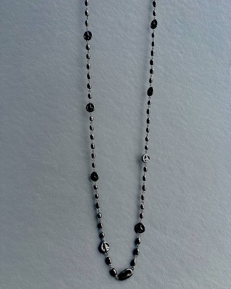 Un sautoir long et fin en perles de céramique entrecoupées de motifs peace and love discrets en perles de céramique noire
