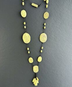 Un collier en perles de céramiques jaunes pales jouant sur les contrastes de tailles de perles et de surface avec des motifs floral