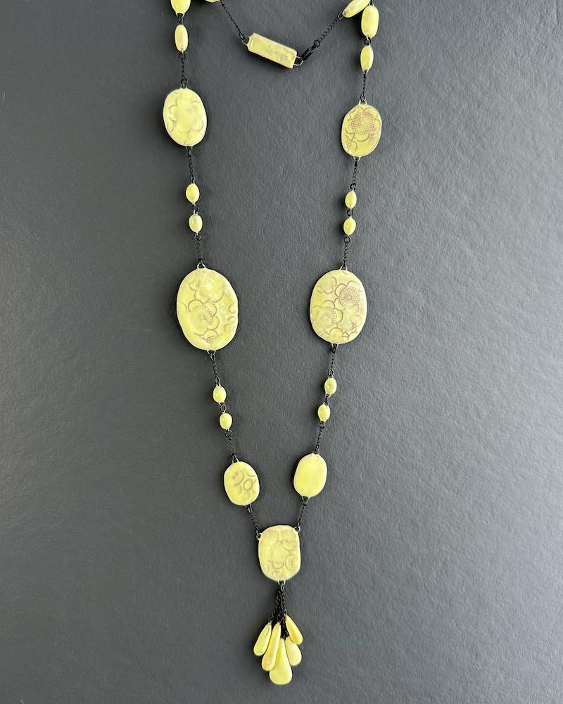 Un collier en perles de céramiques jaunes pales jouant sur les contrastes de tailles de perles et de surface avec des motifs floral